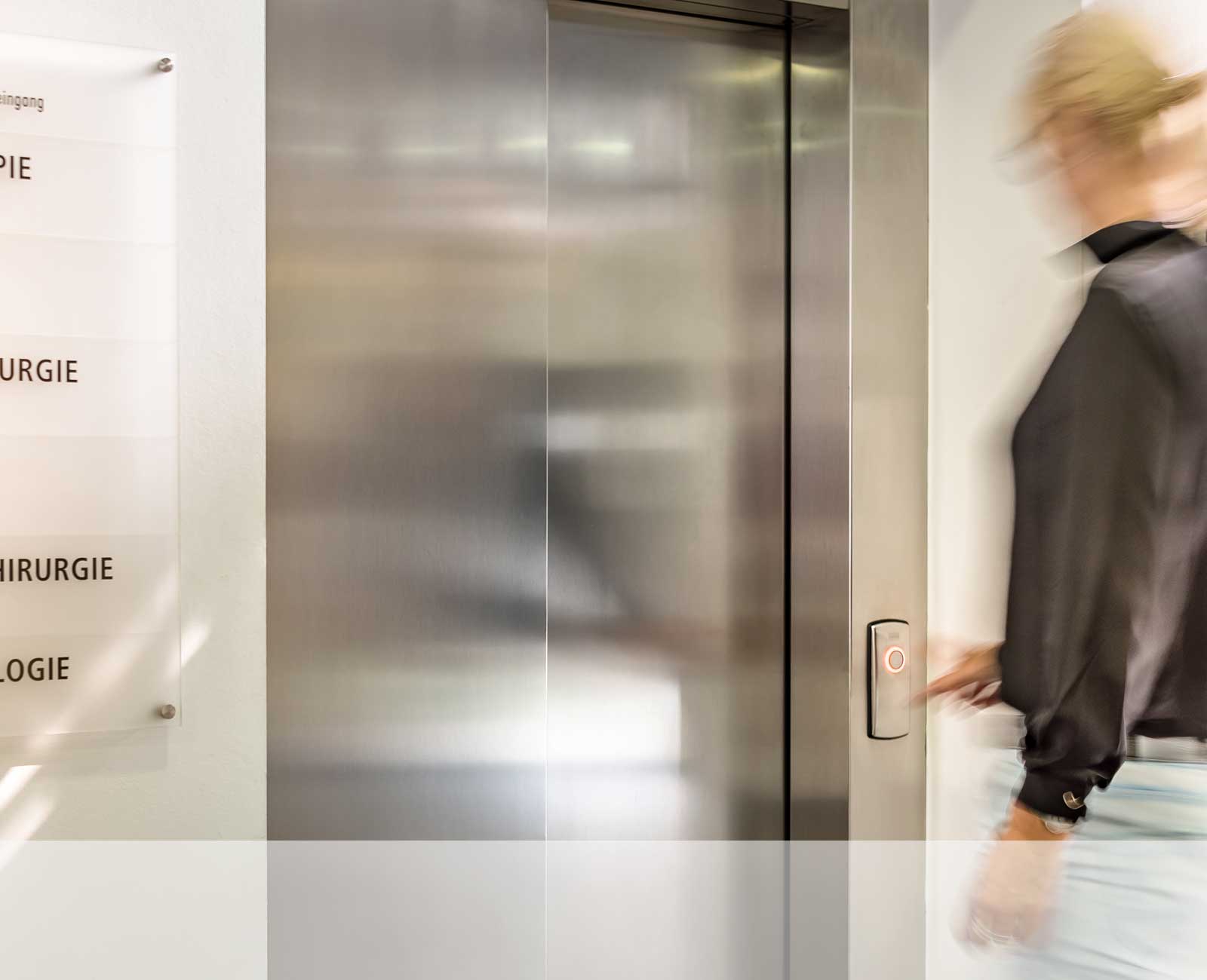 Eine Person steht vor einem Aufzug und drückt auf die Aufzugstaste.