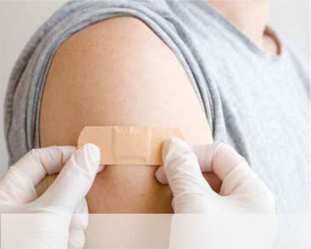 Zwei Hände mit Gummihandschuhen kleben ein Pflaster auf einen Oberarm.