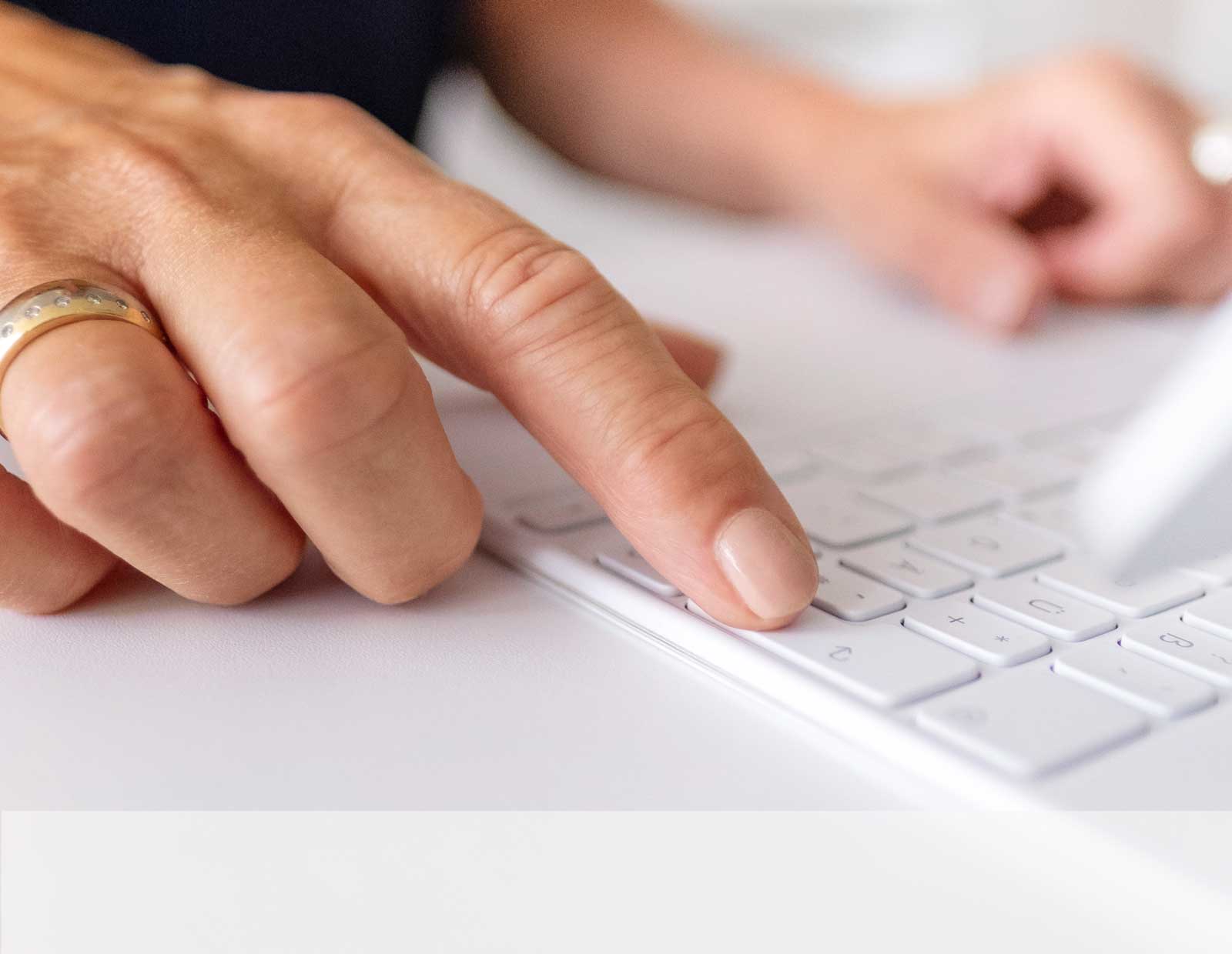 Eine Person sitzt vor einem Computer und tippt mit dem Finger auf die Enter-Taste der Tastatur.