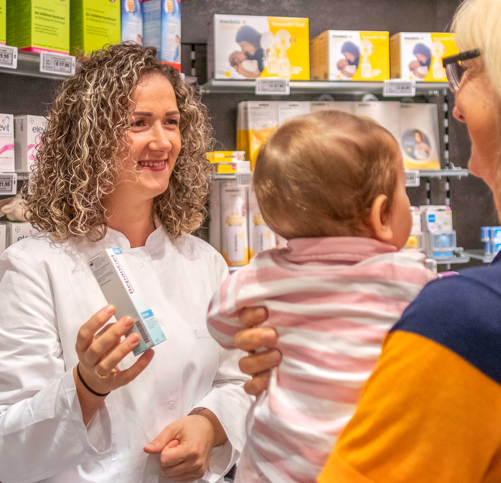 Eine Mitarbeiterin der Salzer Apotheke hält ein Medikament in der Hand und berät eine Kundin.